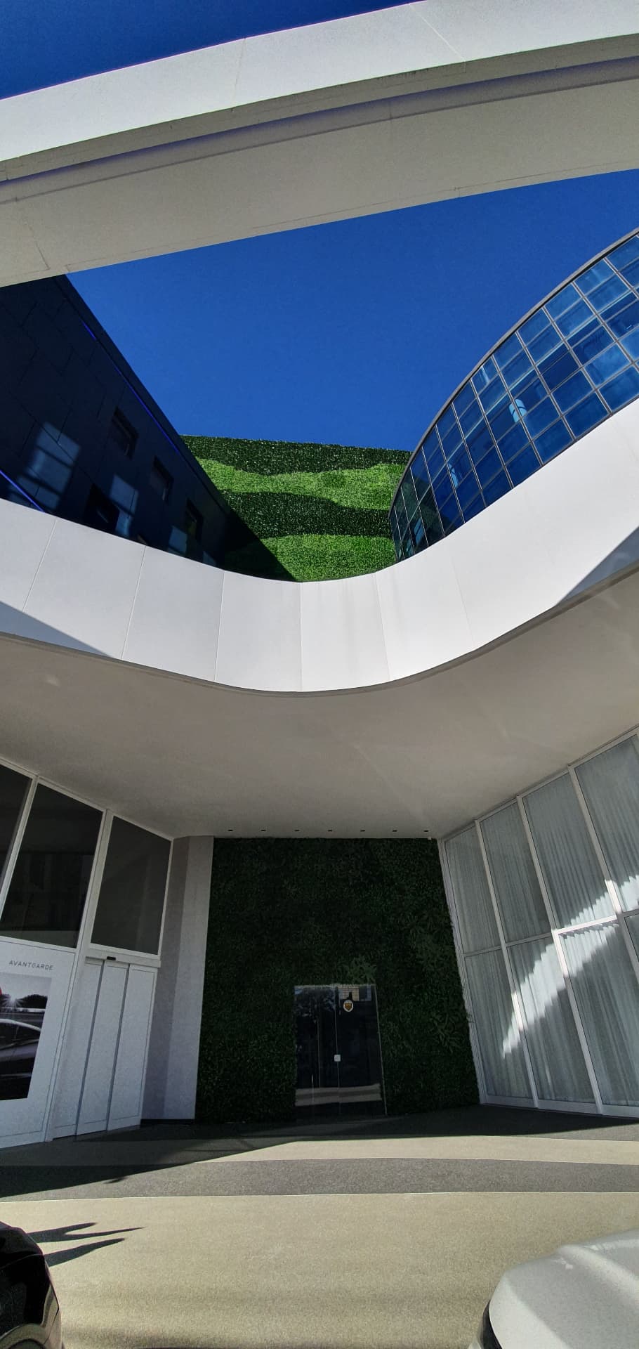 Vão da entrada da Avantgarde Motors visto de baixo, com a parede verde interna e o painel da fachada ao fundo