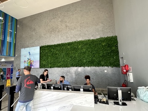 Recepção da AeC com faixa horizontal de jardim preservado sobre parede de concreto e videowall à esquerda