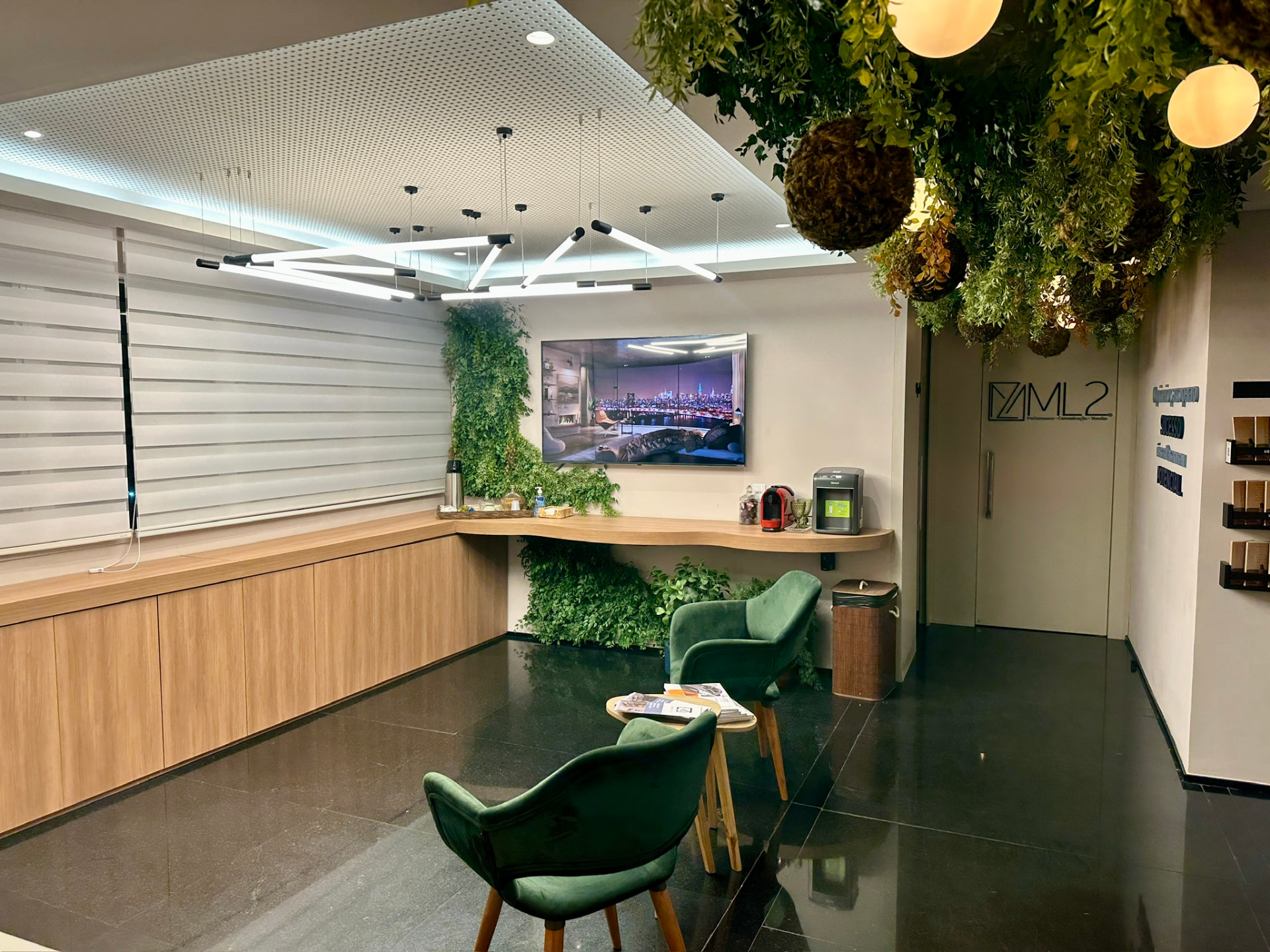 Recepção e lounge da ML2 Company com teto de plantas preservadas, painel verde, TV e bancada de madeira