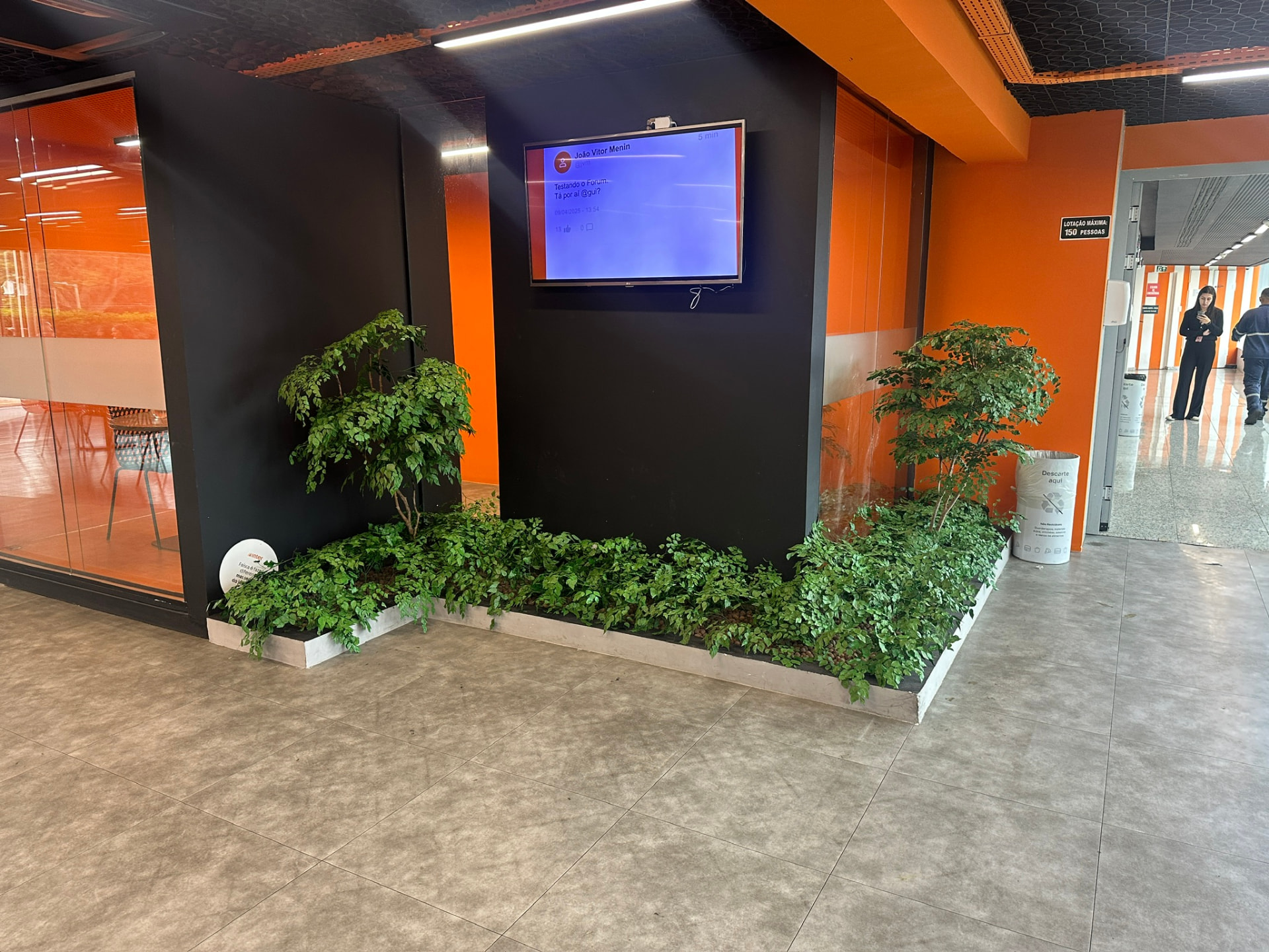 Jardineira com árvores e forração verde no hall do Banco Inter, junto ao painel de vídeo
