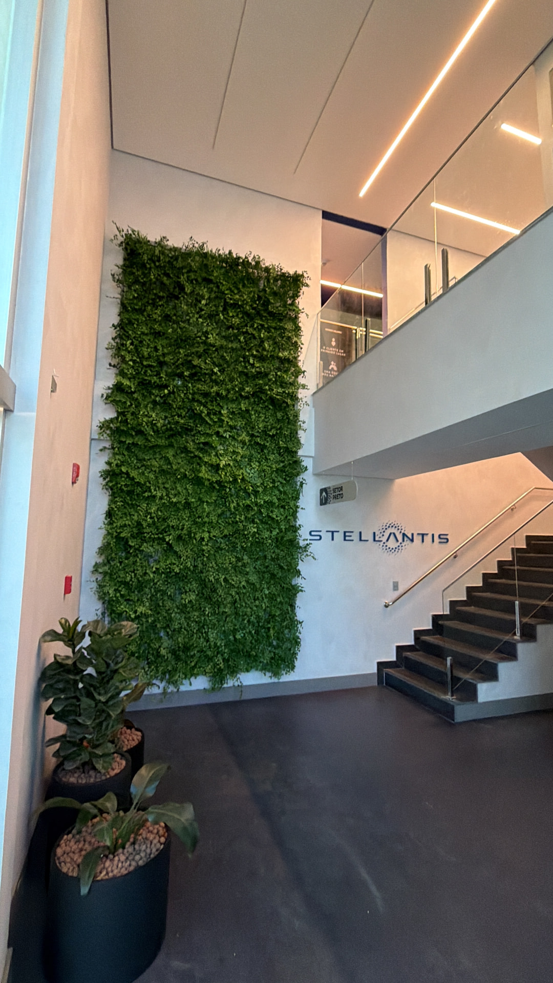 Lobby da Stellantis em Betim com painel preservado, vasos de ficus e escada de acesso