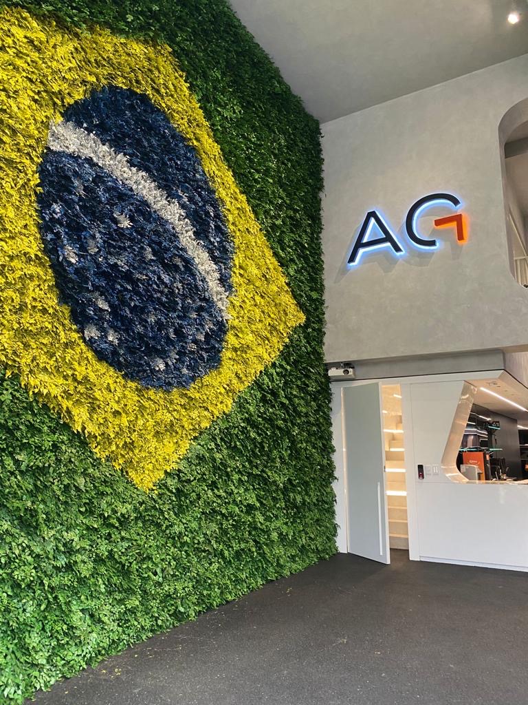Vista lateral da bandeira do Brasil em plantas preservadas ao lado do letreiro iluminado da Avantgarde Motors