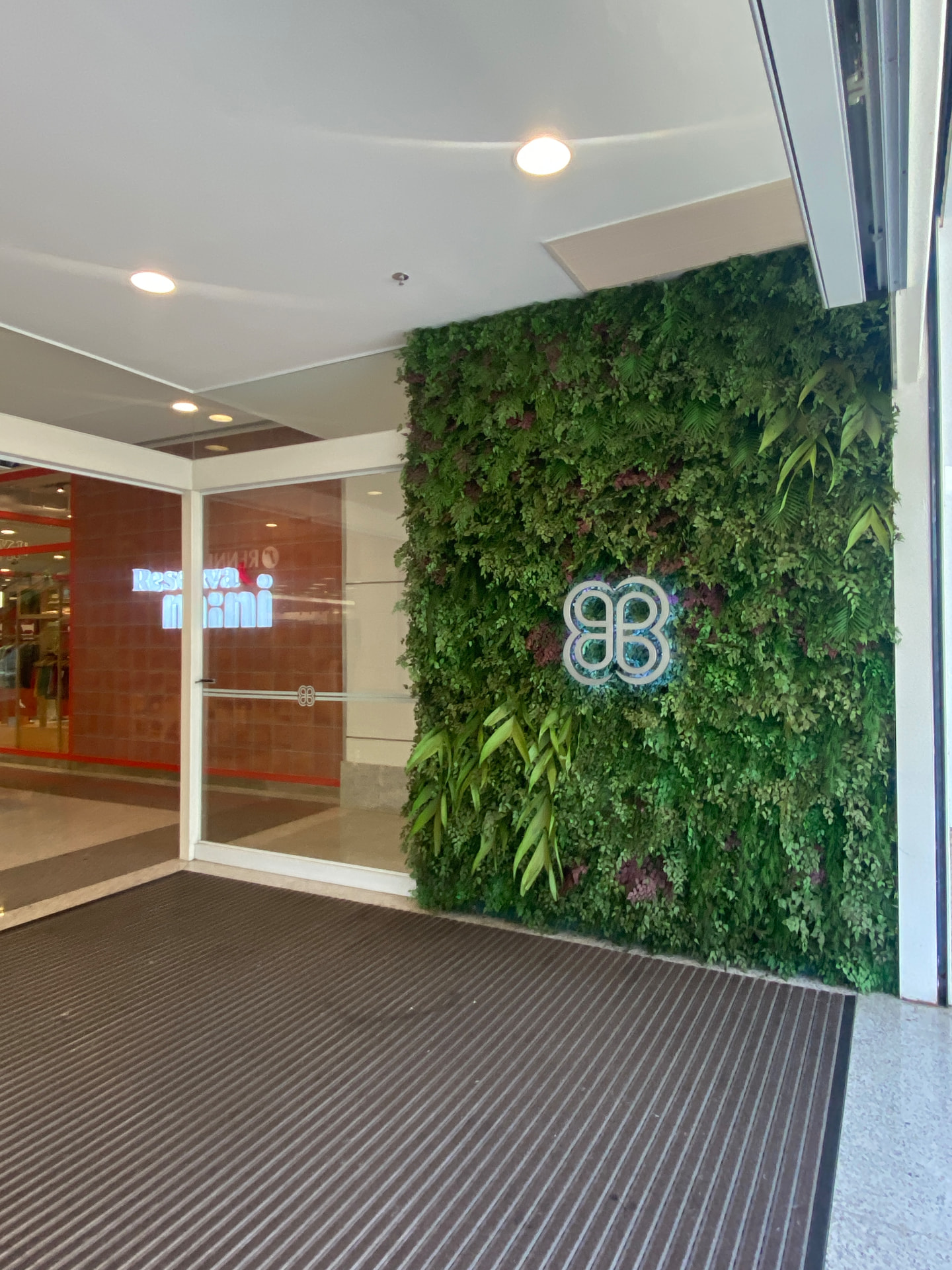 Entrada em shopping · logo iluminada sobre o painel