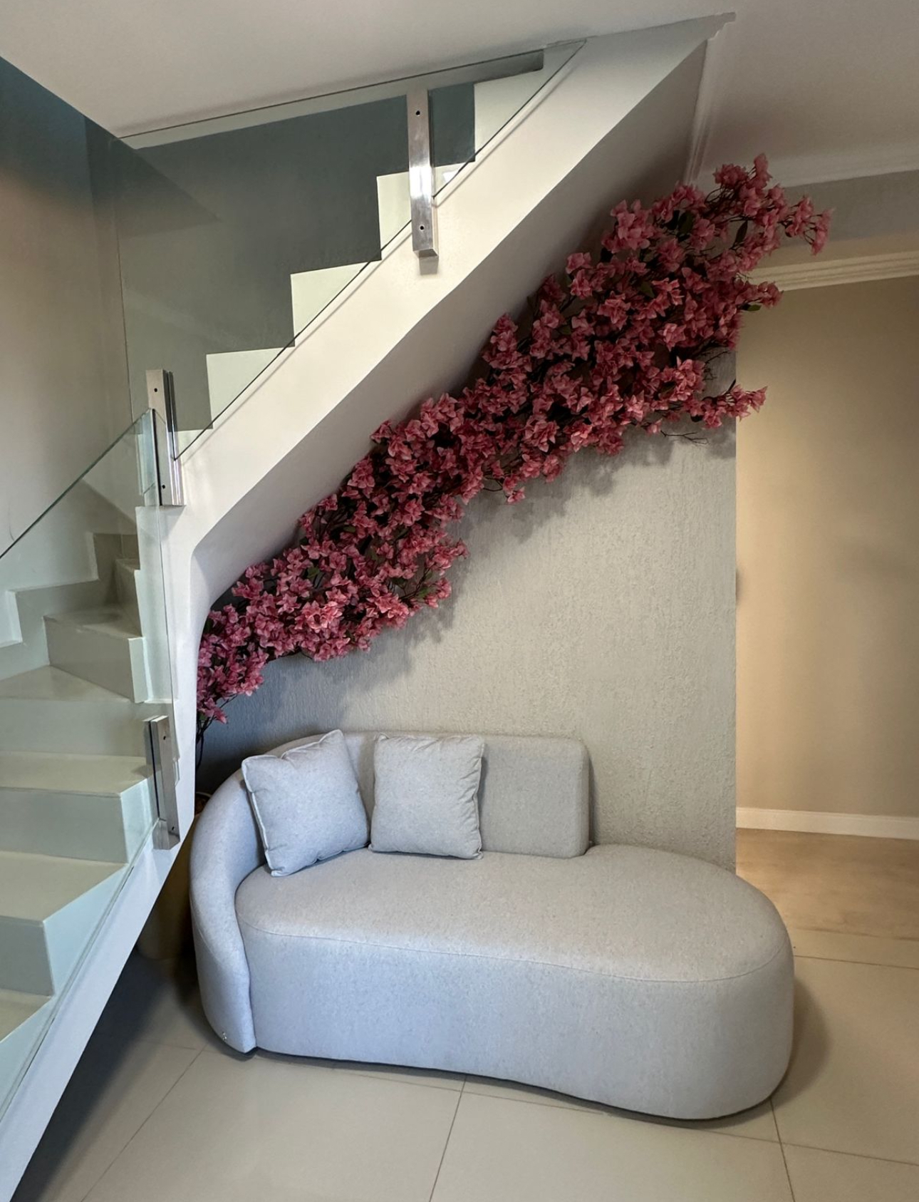 Cascata de bougainville rosa acompanhando o vão da escada sobre sofá curvo