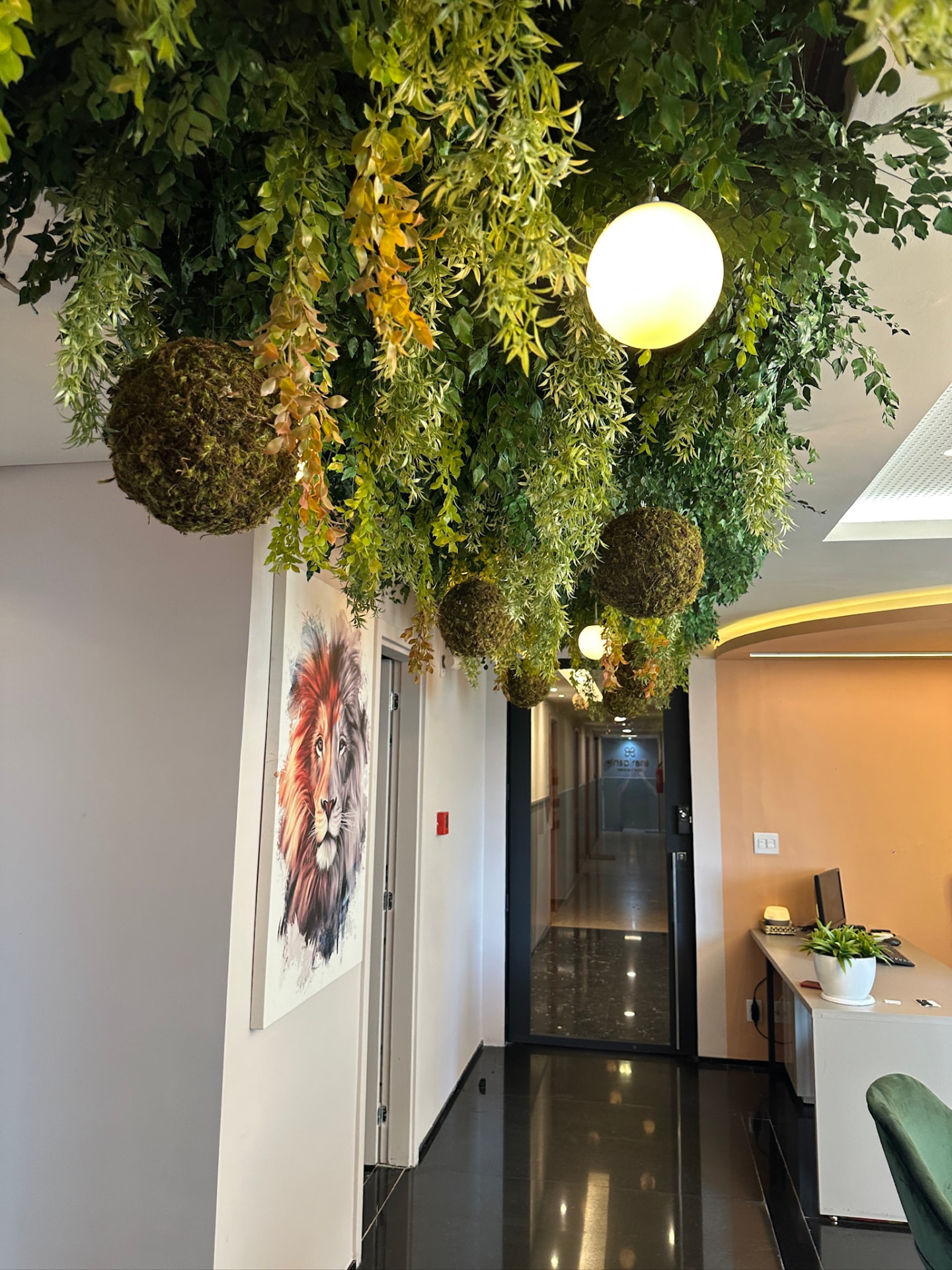 Corredor imersivo da ML2 Company com teto de plantas preservadas, bolas de musgo e quadro de leão