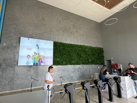 Hall de entrada da AeC com catracas, videowall e faixa de folhagem preservada na parede de concreto