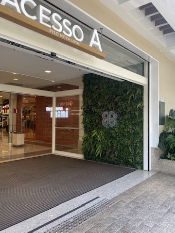 Acesso A do BH Shopping, piso Nova Lima, com painel de plantas preservadas e logotipo aplicado ao lado da porta