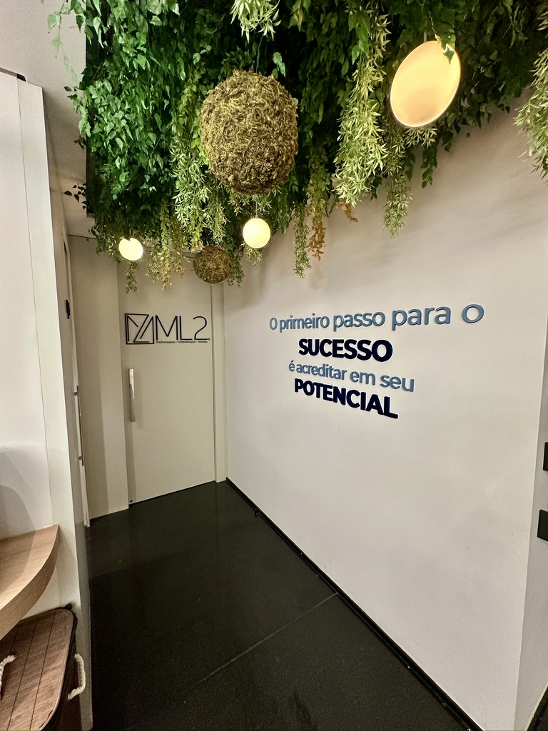 Parede institucional da ML2 Company sob teto de plantas preservadas com bolas de musgo e luminárias