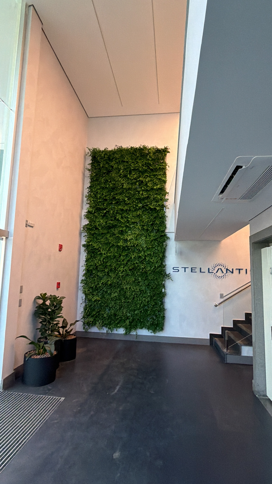 Jardim vertical preservado de pé-direito duplo ao lado do letreiro Stellantis no lobby de Betim