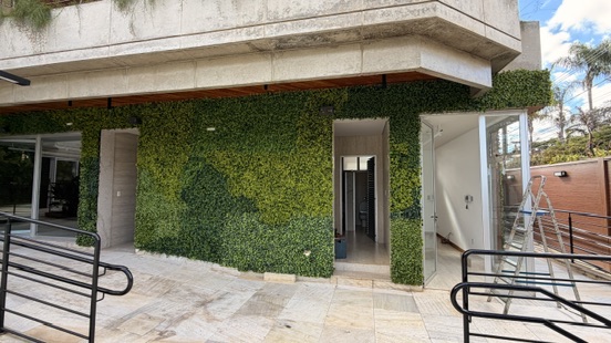 Fachada da JMM Tech revestida em parede verde permanente sob laje de concreto, com acessos de vidro