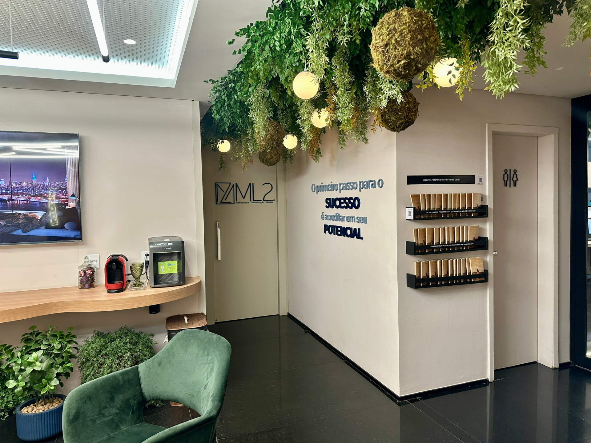 Lounge da ML2 Company com teto de plantas preservadas, luminárias esféricas e parede com a marca ML2