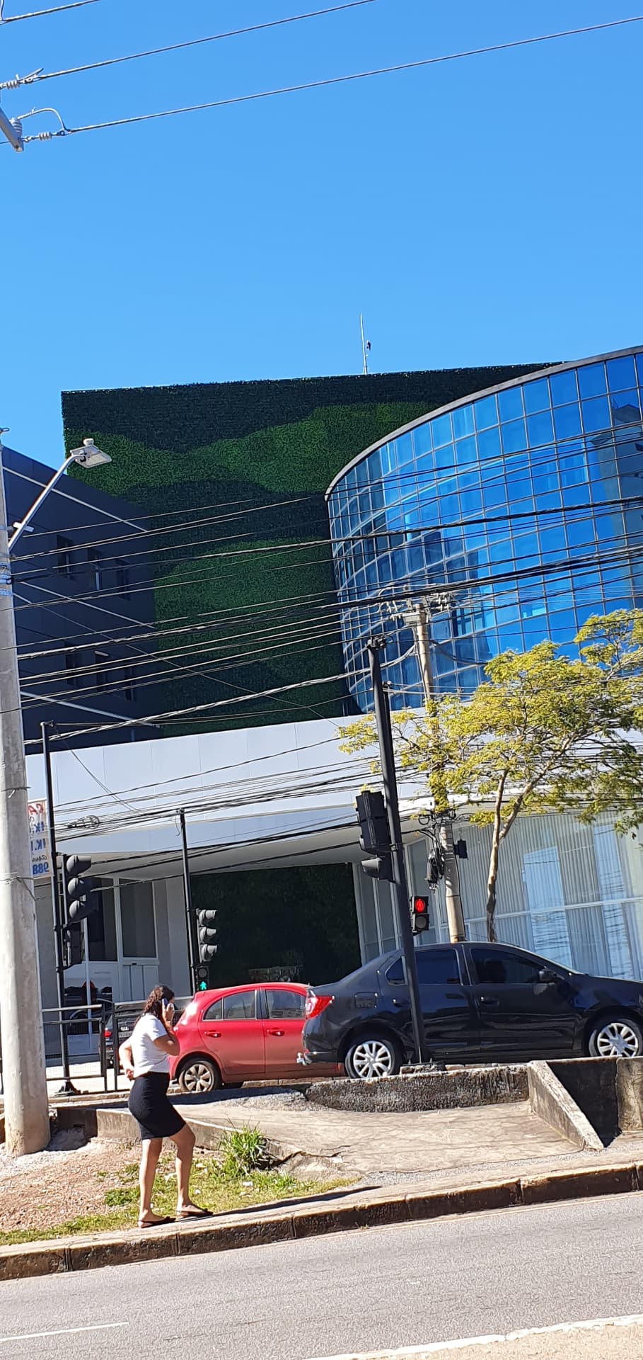 Vista ampla da fachada da Concept Store da Avantgarde Motors com o painel verde ao lado do volume de vidro azul