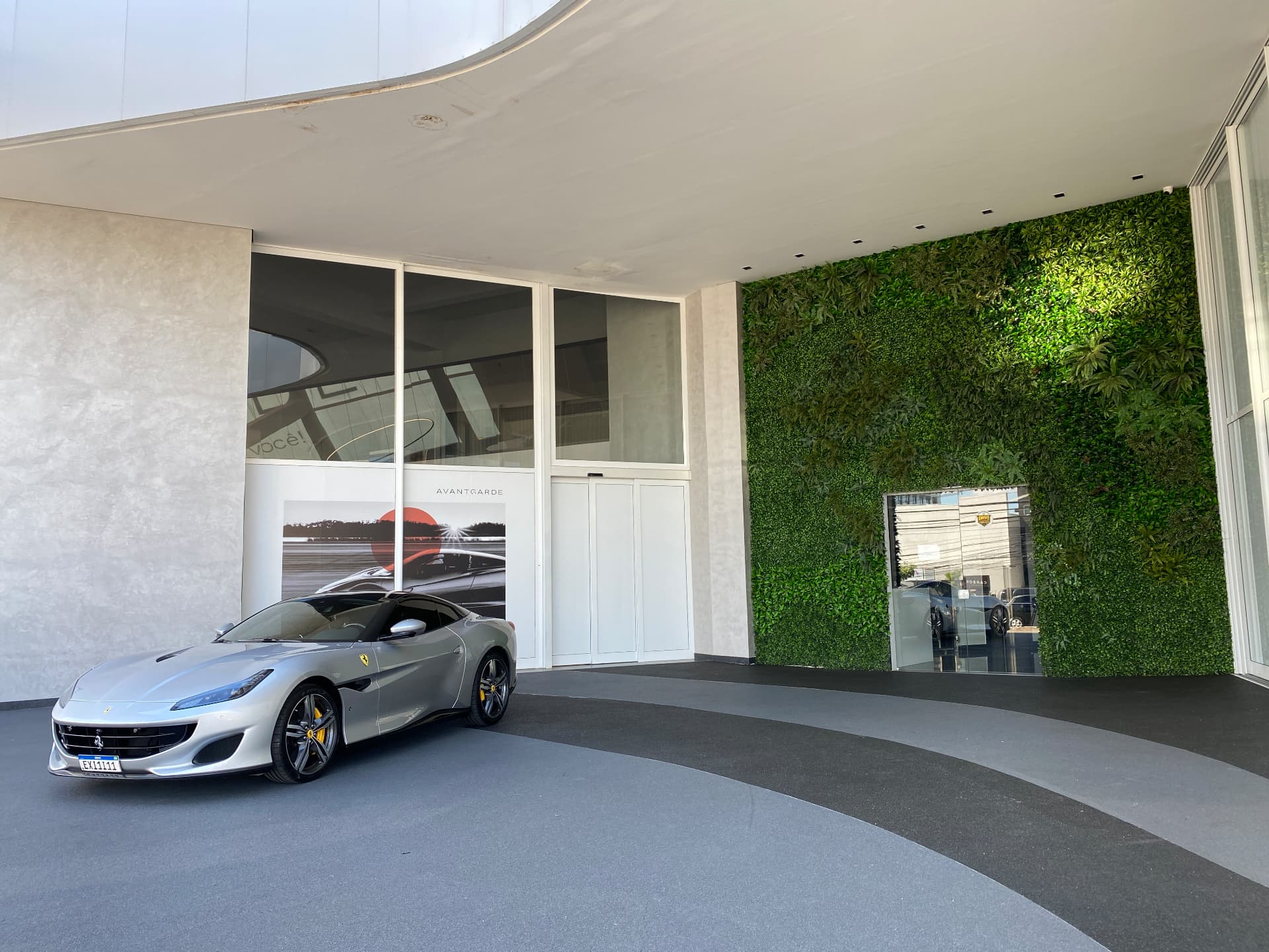 Ferrari prata estacionada na entrada coberta da Avantgarde Motors diante da parede verde permanente de pé-direito duplo