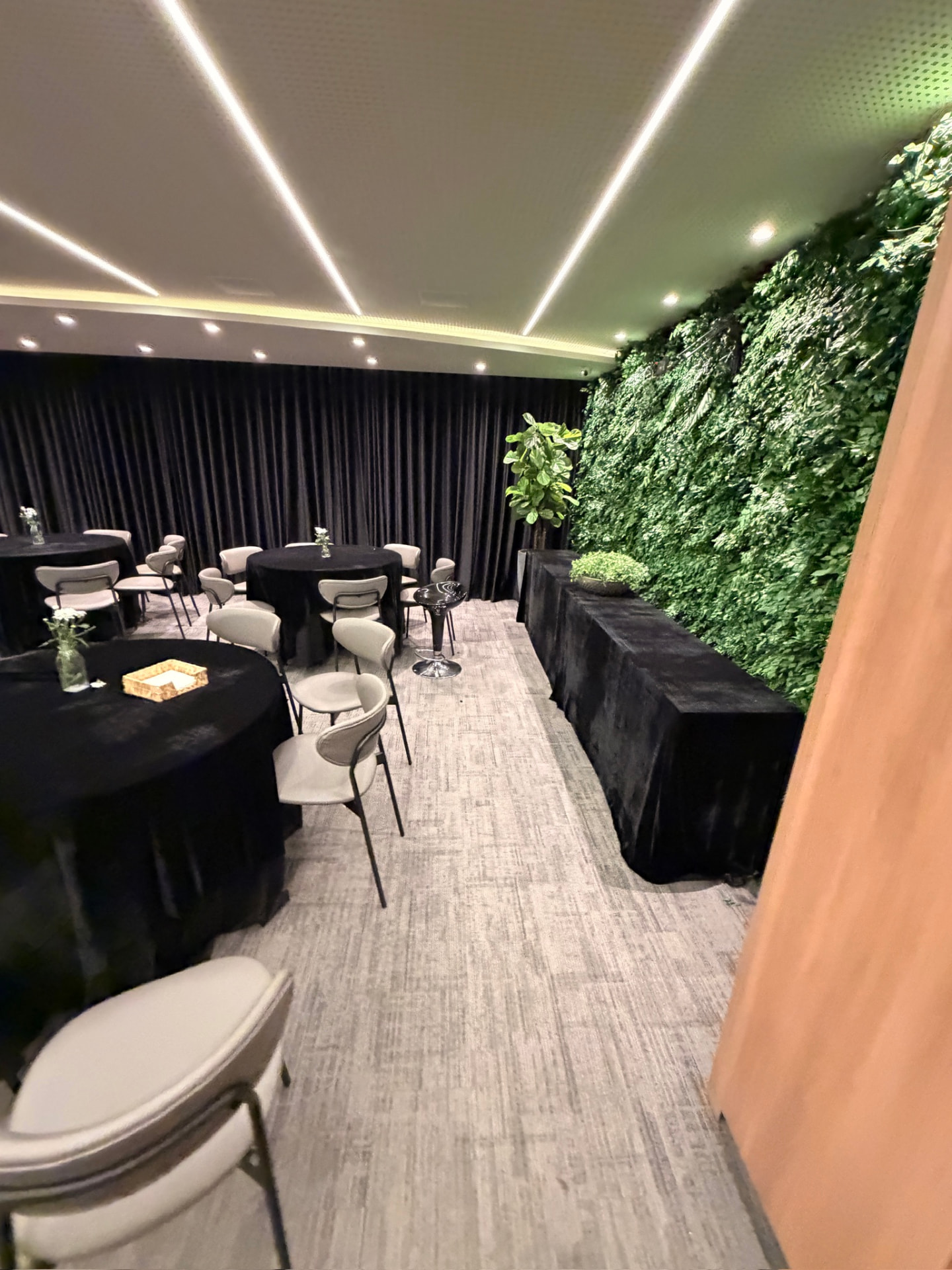 Auditório da ML2 Company montado para evento, com mesas redondas e jardim vertical preservado ao longo da parede