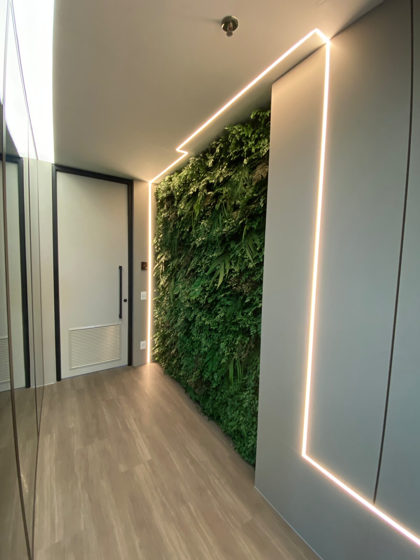 Jardim vertical preservado emoldurado por fita de LED em corredor de acesso