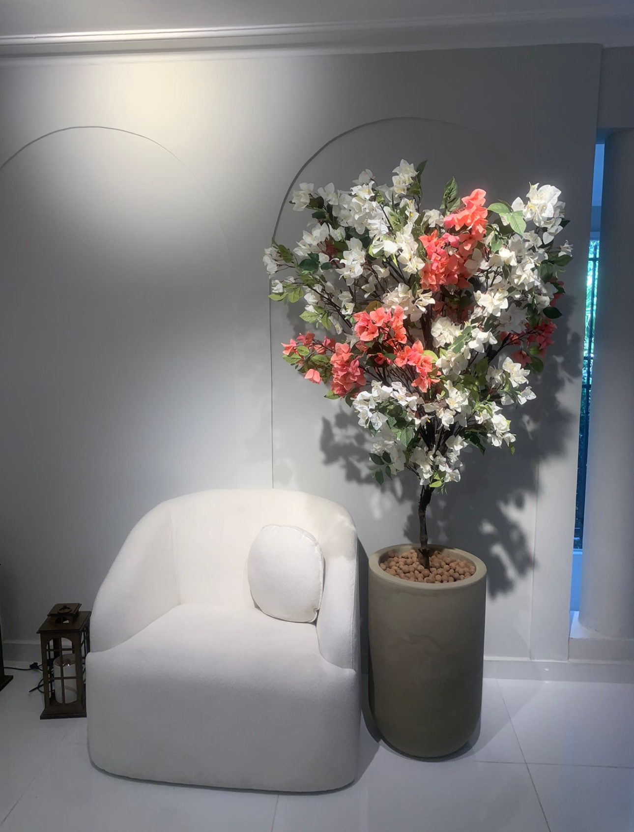 Bougainville branca e coral em vaso cilíndrico ao lado de poltrona branca em sala de espera