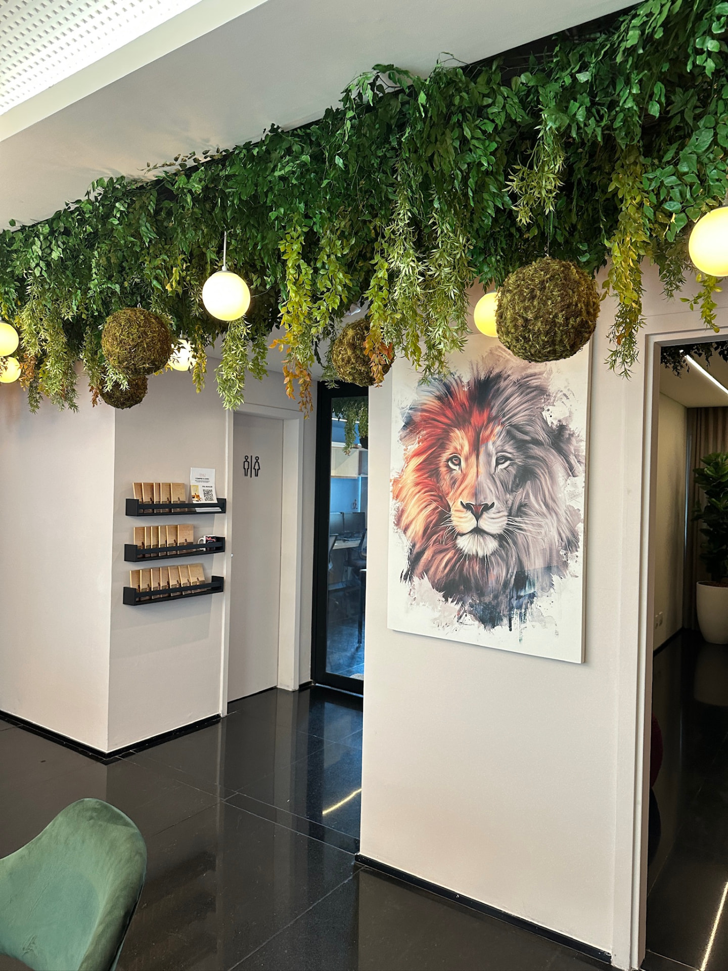 Área de espera da ML2 Company com teto vegetal, luminárias e quadro de leão
