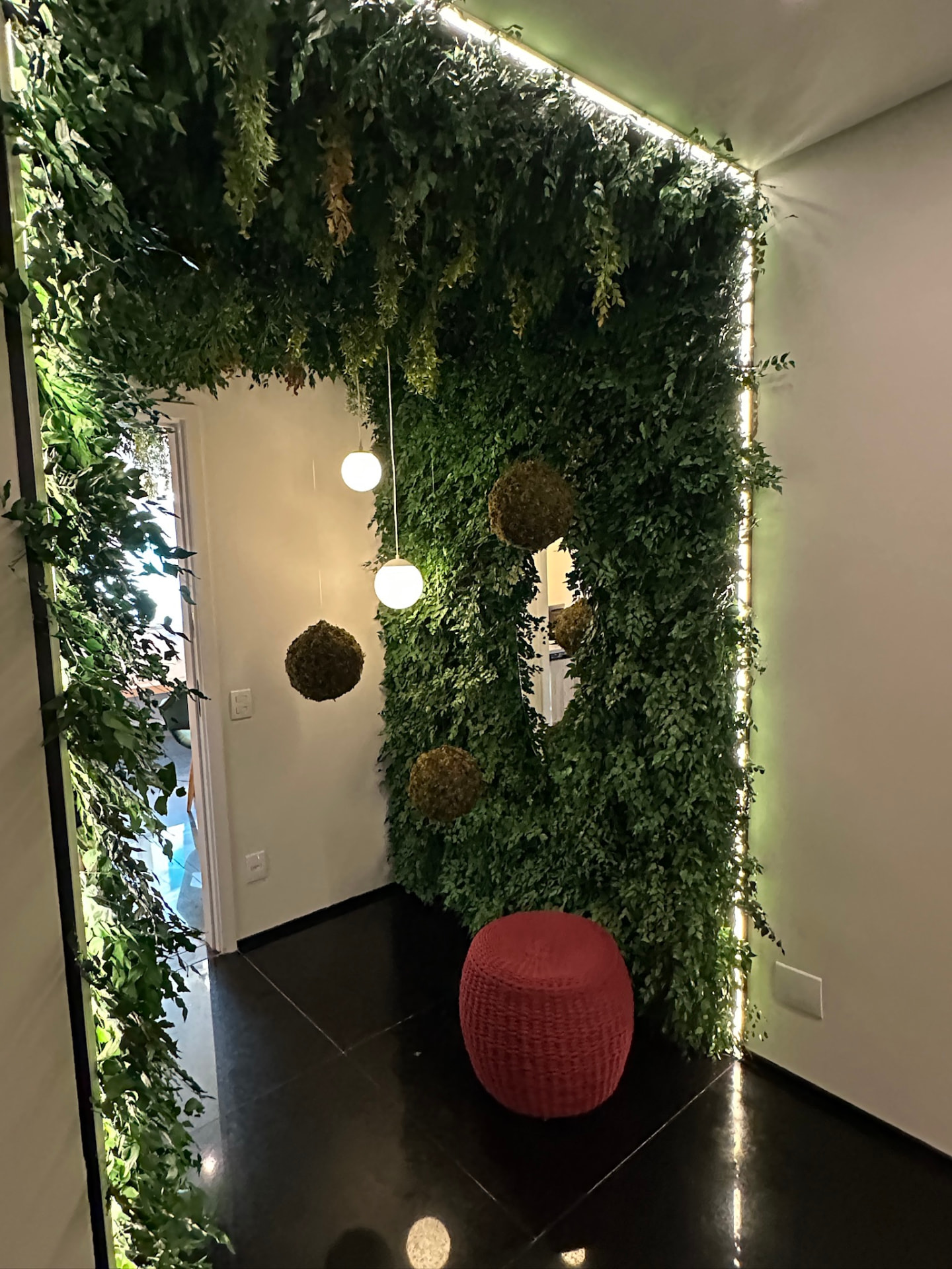 Painel vertical preservado iluminado na ML2 Company com esferas de musgo e pufe vermelho