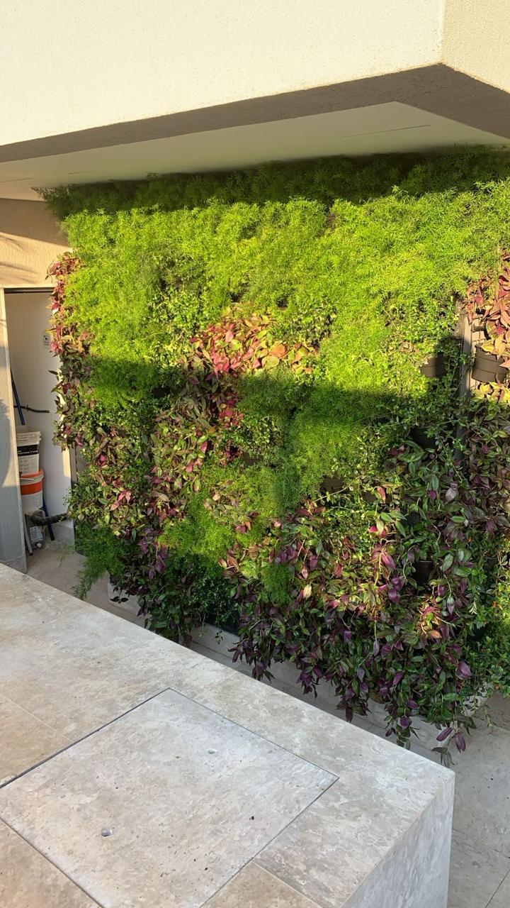 Jardim vertical natural em plena luz com folhagens verdes, rosas e roxas