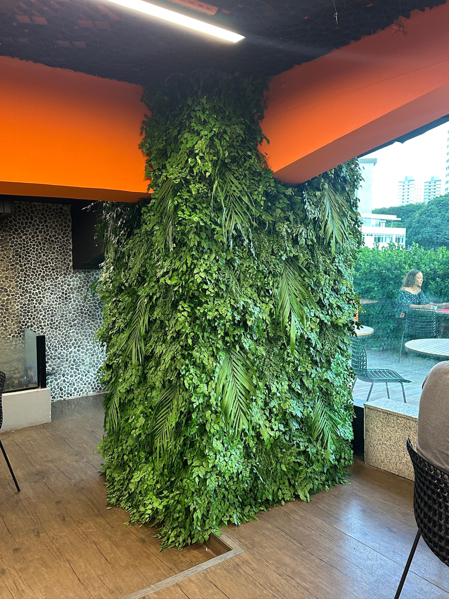 Coluna e parede verde preservada do Banco Inter refeita com placa ecológica e folhas grampeadas, junto à área externa envidraçada