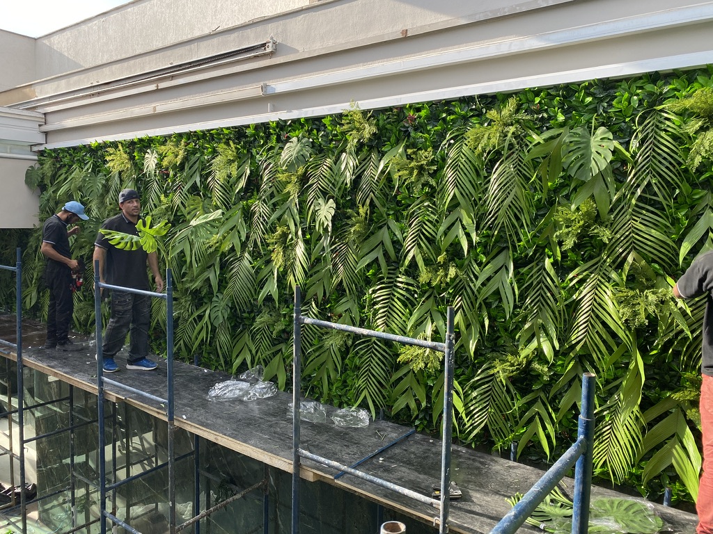 Equipe da Casa do Jardim aplicando folhas preservadas sobre o fundo permanente da parede verde da Cobertura LFP